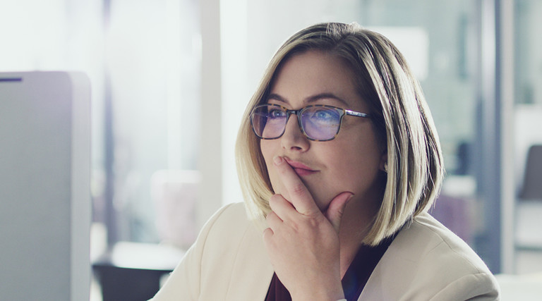 Woman CIO with glasses and dirty blonde hair sitting at her computer and thinking