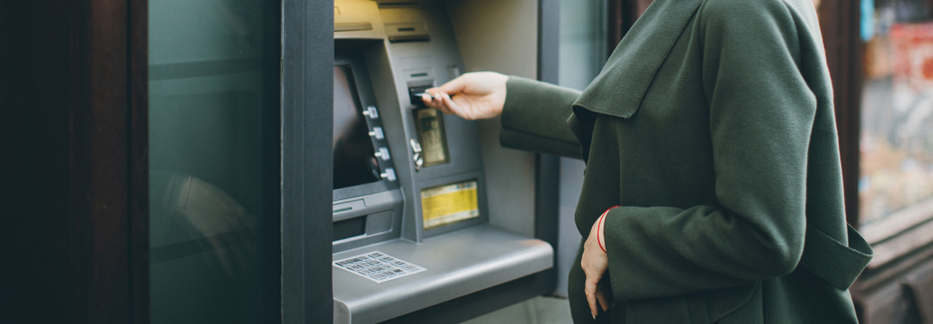 Woman in a green coat using an ATM 