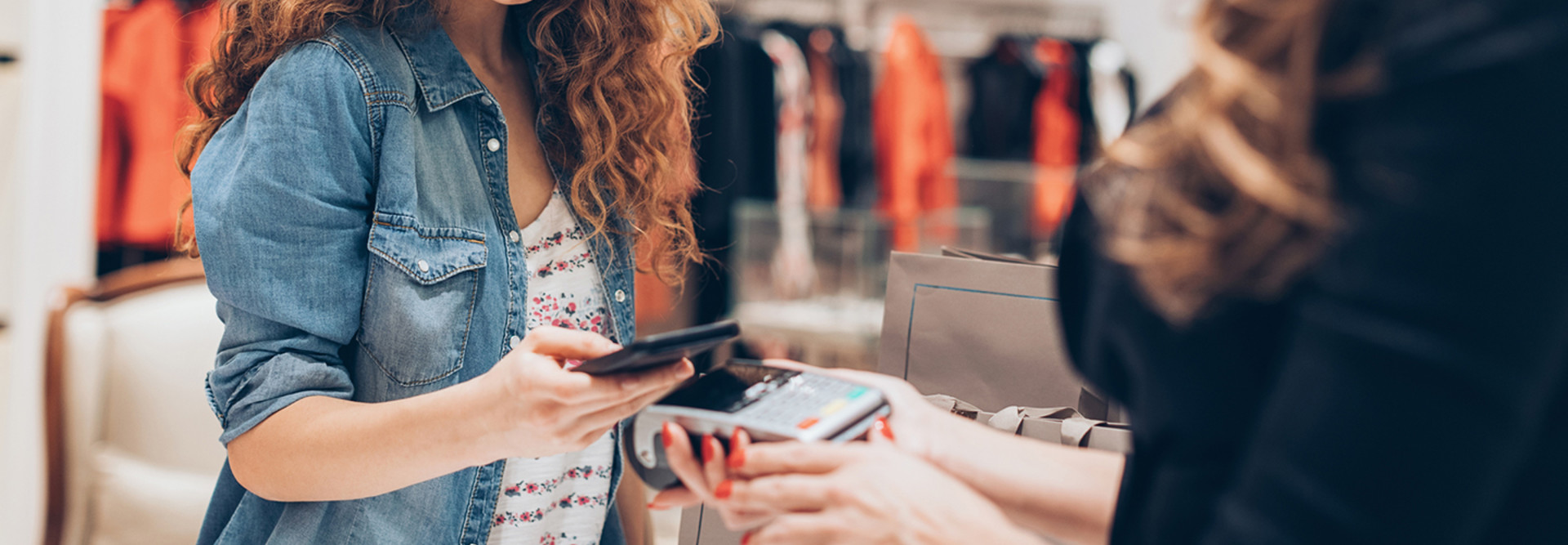 Woman using her smartphone to pay for clothing at a retail store 