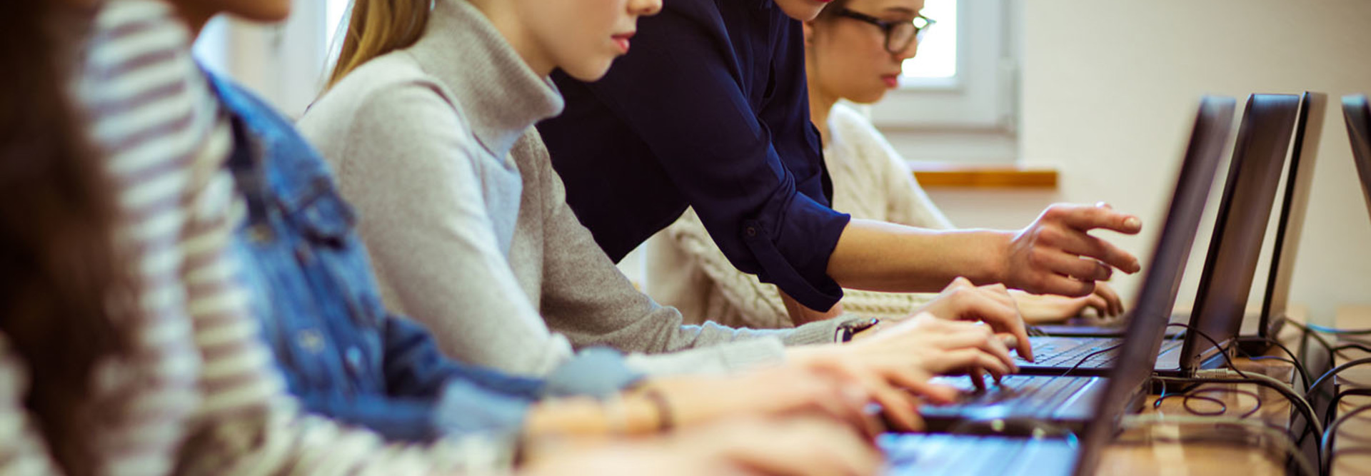 Group of women coding on laptops. Focus on hands of female students typing on laptop keyboard in a computer lab.