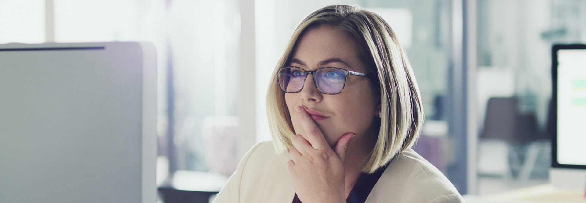 Woman CIO with glasses and dirty blonde hair sitting at her computer and thinking