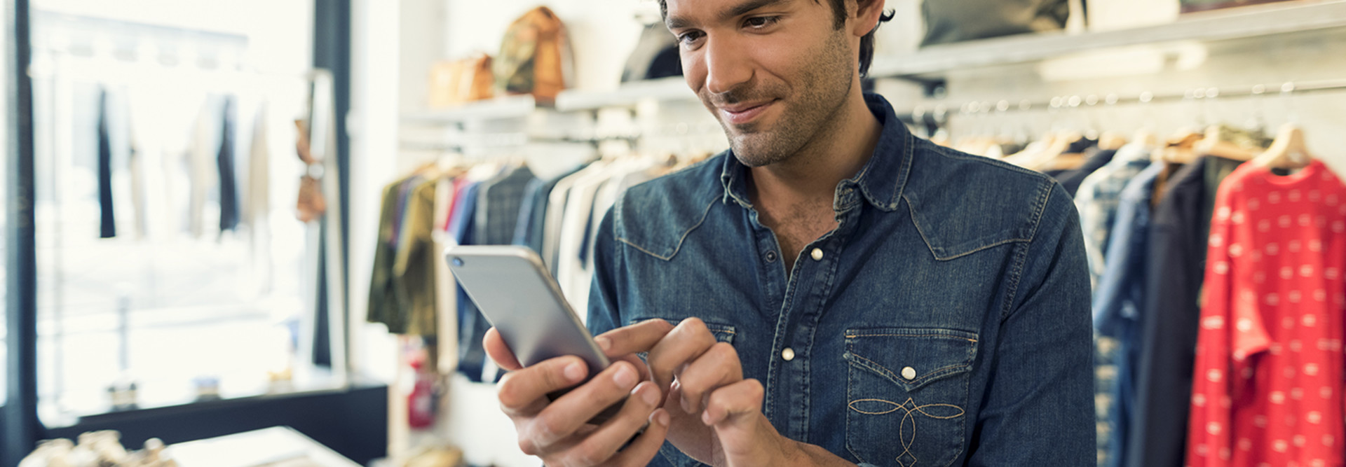 A male shopper standing in a store uses a retail mobile app to learn more information about products that interest him