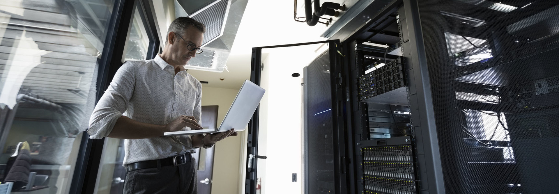 Male Caucasian IT technician using laptop in server room