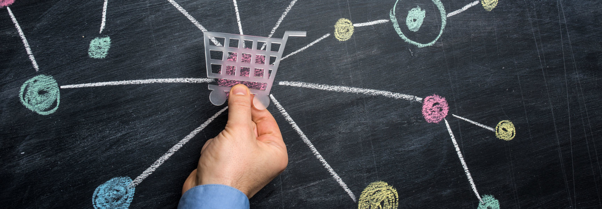 Man holding a shopping cart symbol shape over the central node of a multicoloured network drawn on blackboard