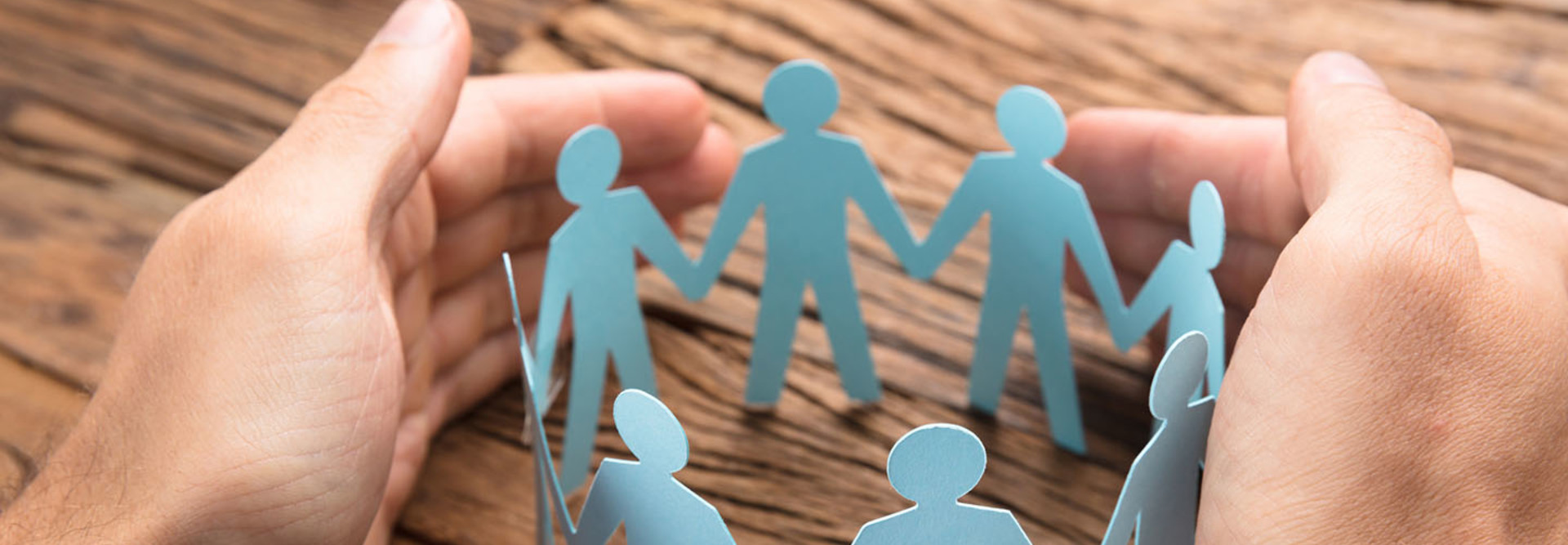 Cropped image of businessman's hands covering paper team on wooden table