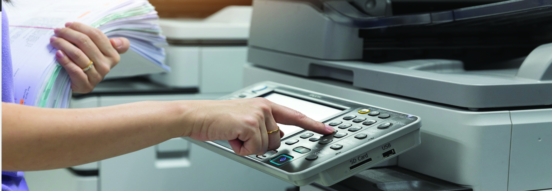 woman holding a stack of papers and pushing buttons on a copier