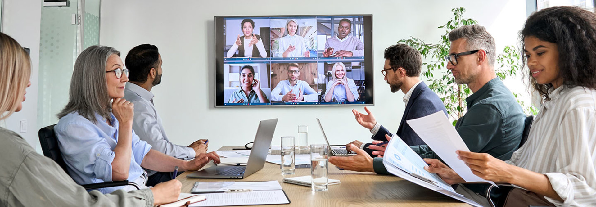 Diverse employees on online conference video call on tv screen in meeting room.