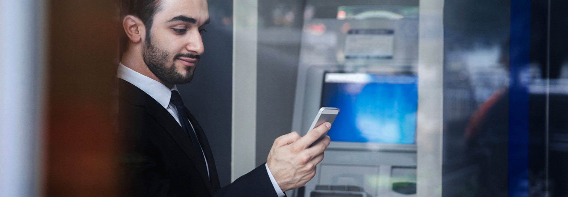 Man using smartphone by bank ATM 