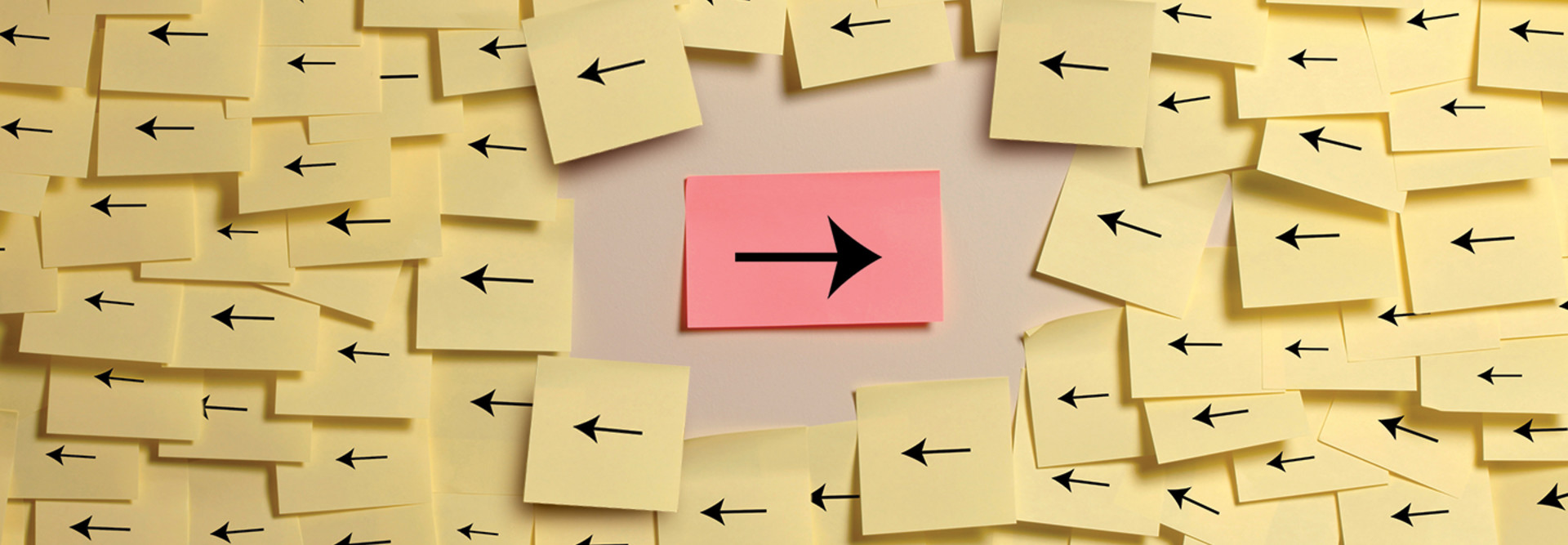 A right-facing arrow on a red post-it note amid a sea fo left-facing arrows on yellow post-it notes