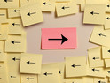 A right-facing arrow on a red post-it note amid a sea fo left-facing arrows on yellow post-it notes