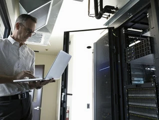 Male Caucasian IT technician using laptop in server room