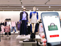 hand holding smart phone in front of store mannequins