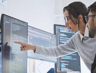 two people look at computer monitors