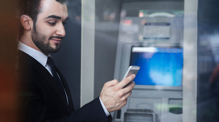 Man using smartphone by bank ATM 