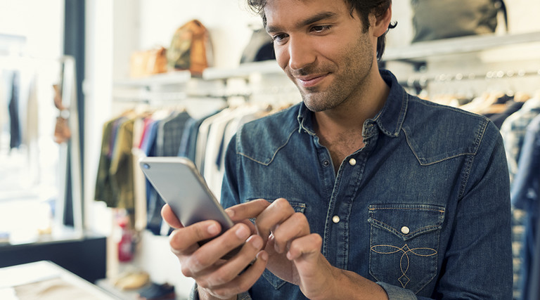 A male shopper standing in a store uses a retail mobile app to learn more information about products that interest him