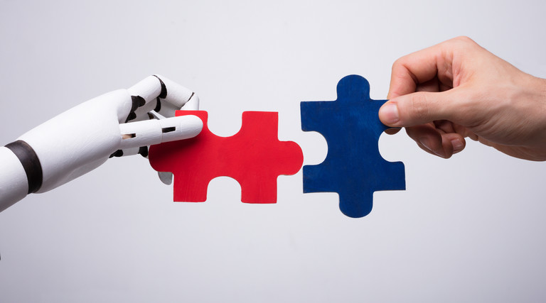 Robot and human hands putting puzzle pieces together