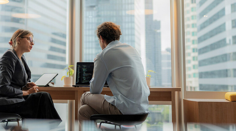 Adviser in modern office working on computer while speaking with clients