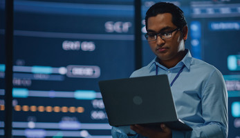 IT leader with laptop in room full of data visualizations 